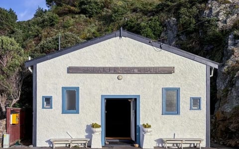 White rendered hall with blue trim and timber sign above entrance