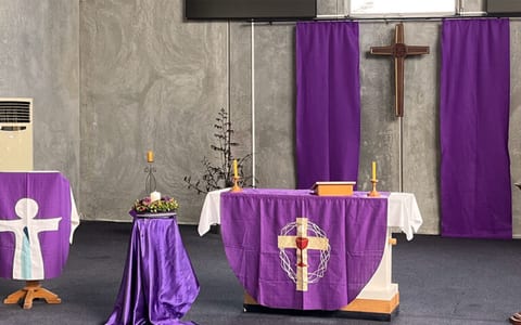 Church sanctuary interior with altar table draped in purple, wooden cross, and candles
