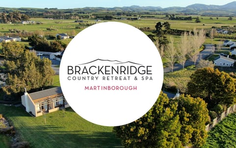 Aerial view of low-rise white buildings set among green farmland, rolling hills and flat plains extending behind, venue logo overlaid