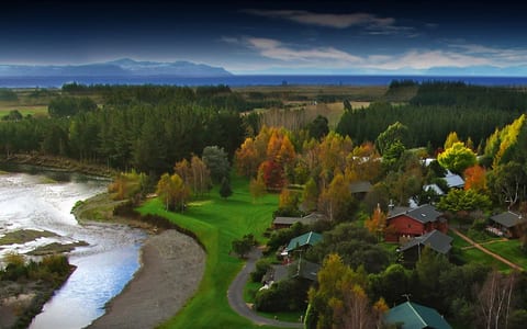 Aerial view of lodge buildings among autumn trees beside a river, lake in background