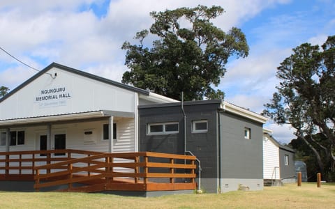 Small white memorial hall with timber deck, ramp and dark addition at rear