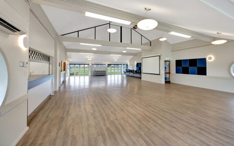 Empty community hall with timber floor, high ceiling, and projection screen