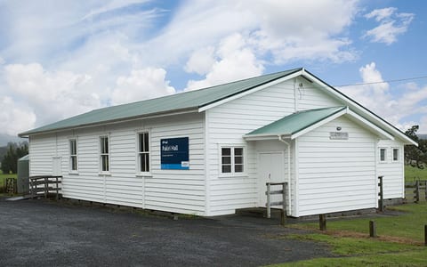 White weatherboard hall with green metal roof, gravel car park, and paddock setting