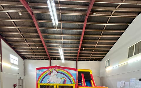 Open sports hall with metal roof structure, bouncy castle, and scattered balloons