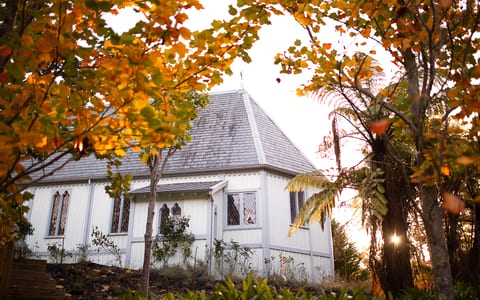 White timber chapel with steeply pitched roof and decorative bargeboards, framed by autumn trees