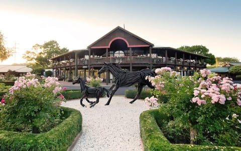 Dark timber two-storey pavilion with a veranda, flanked by formal gardens and horse sculptures
