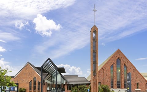 Red brick church complex with tall open-frame spire, pointed windows, and glass entry canopy