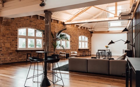 Brick-walled loft interior with exposed timber trusses, timber floor, bar tables and lounge seating