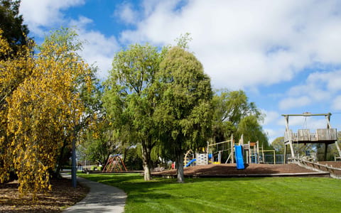 Park with playground equipment and mature trees under blue sky
