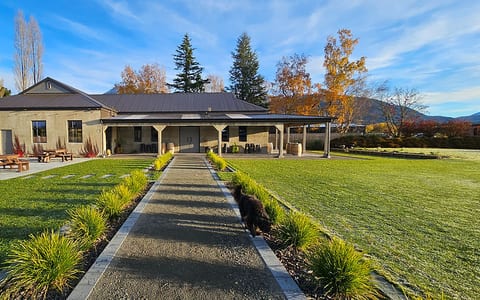 Single-storey rendered venue building with covered veranda, gardens, and mountain backdrop