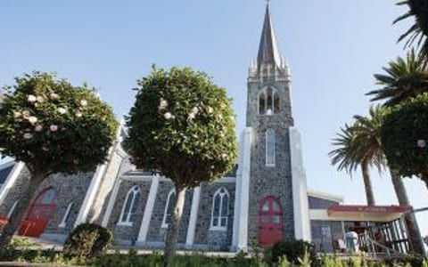 Dark basalt stone church with tall spire, pointed arched windows, and trees in the forecourt