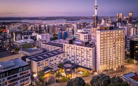 Aerial dusk view of large multi-storey city hotel with illuminated tower and surrounding urban skyline