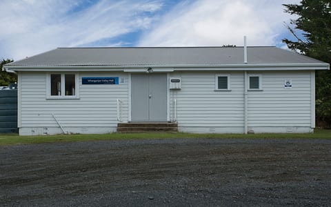 White weatherboard hall with grey iron roof and gravel car park
