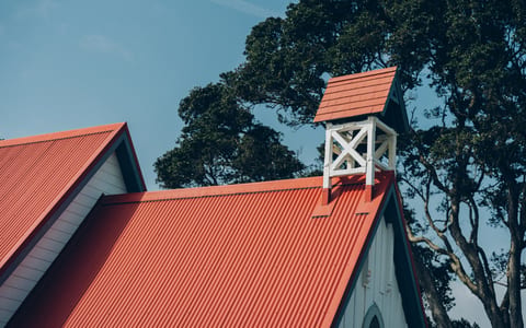 Close-up of timber church roofline with red corrugated iron and small bell tower against blue sky
