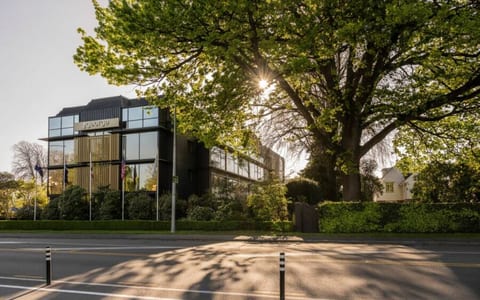 Dark multi-storey building with vertical timber screens, large trees framing the street frontage