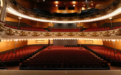Ornate theatre auditorium with red seating, balcony and decorative plasterwork