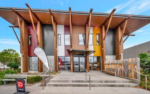 Two-storey community centre exterior with angled timber columns, coloured cladding panels, and covered entry