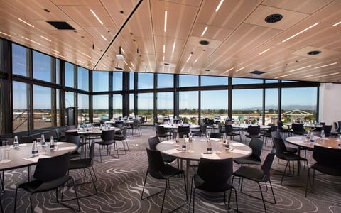 Light timber ceiling event room with round tables and black chairs, floor-to-ceiling windows and open views