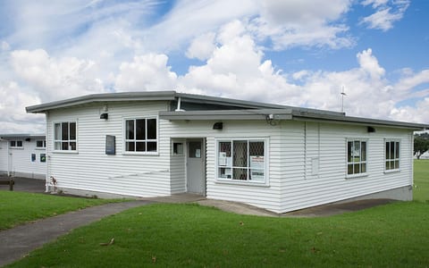 Single-storey white weatherboard community building with lawn