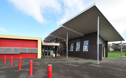 Mid-century community centre with flat canopy roof, dark cladding, and colourful artwork panels