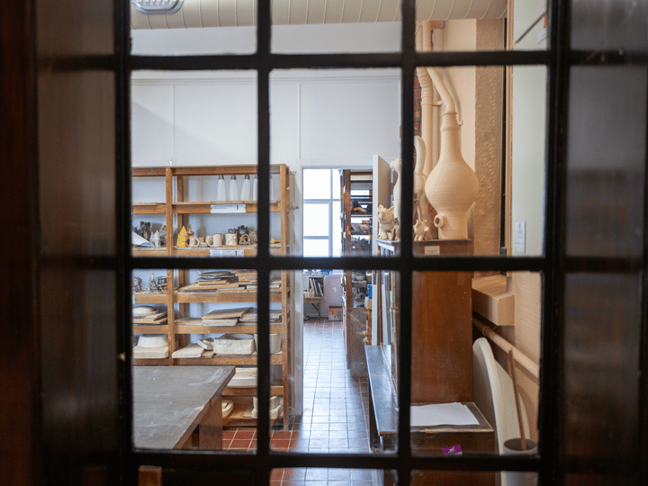 View through glazed door into ceramics workshop with shelving and pottery pieces