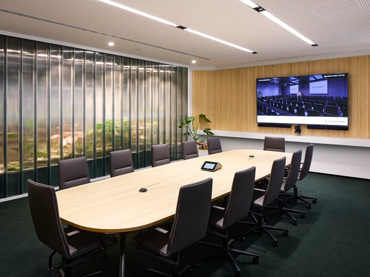 Boardroom with oval timber table, leather chairs, timber louvre wall feature, large screen, and green carpet
