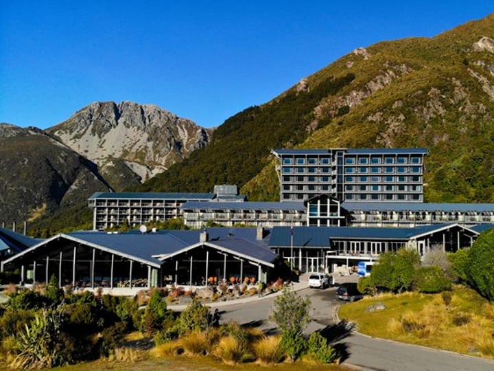 Multi-storey hotel complex with low-pitched roofs set against steep bush-covered mountain slopes