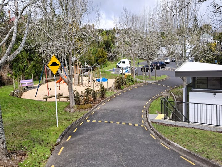 Sealed path through park area with playground equipment and bare trees visible