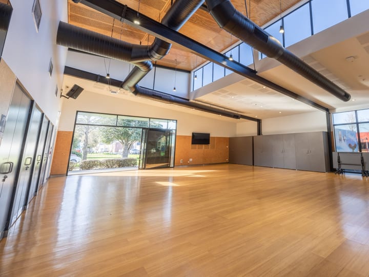 Large open hall with timber floor, exposed duct services, and coloured glazed panels
