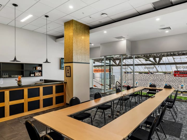 Small meeting room with U-shaped table, black chairs, a bar counter, and glass wall overlooking stadium field