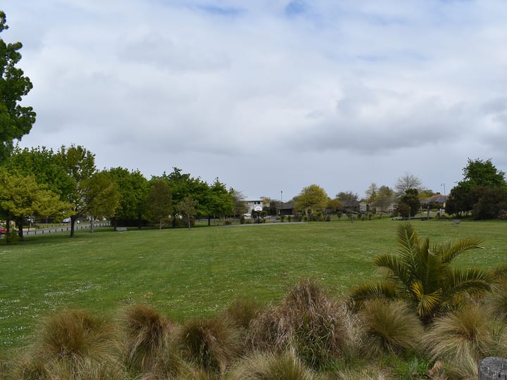 Open grassed reserve with trees and plantings under cloudy sky