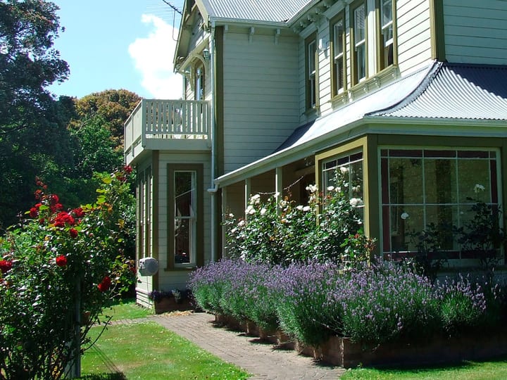 Two-storey villa exterior with a verandah, lavender garden border and mature trees