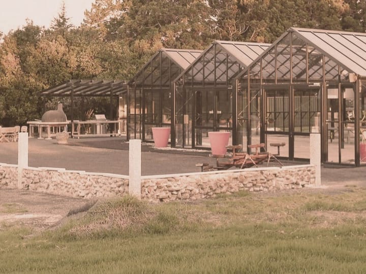 Black steel-framed glasshouse structures with stone wall surround, open rural setting