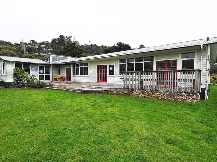White weatherboard hall with red window frames, veranda, and lawn