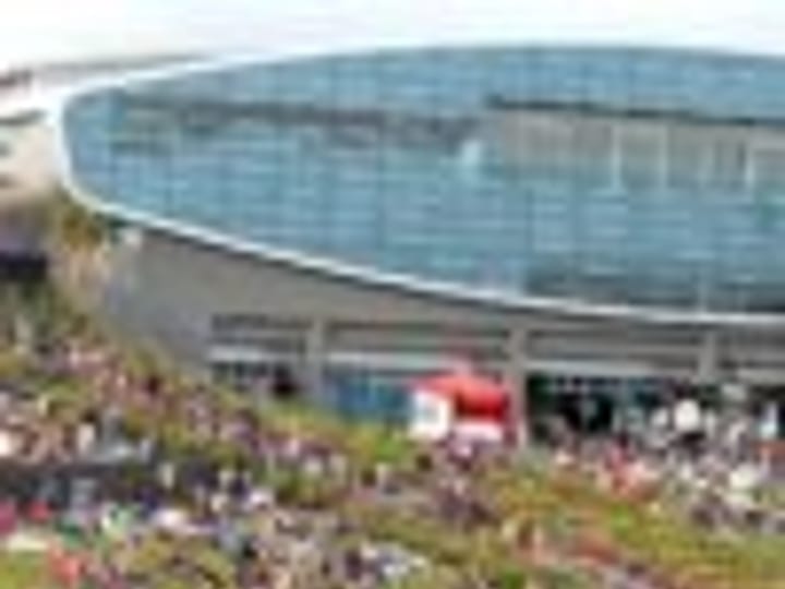Large arena building with crowd on surrounding lawn at outdoor event