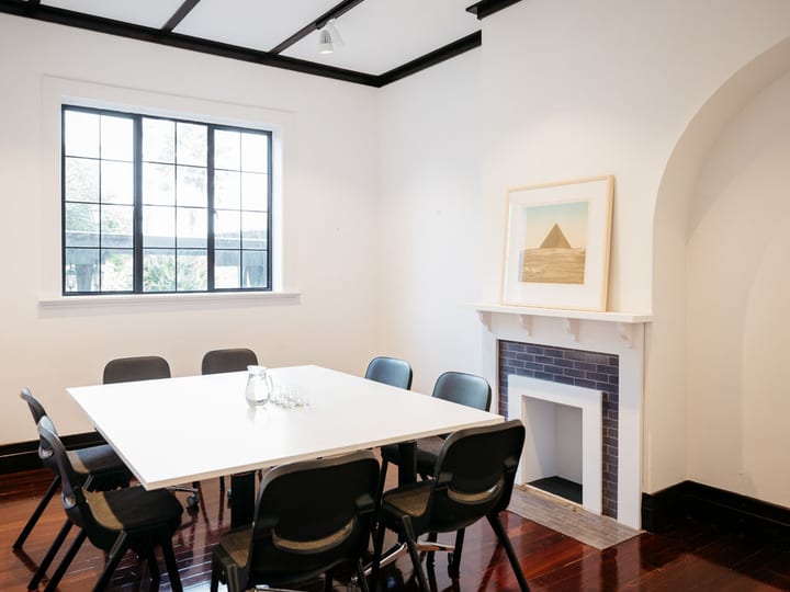 Small meeting room with white table, black chairs, fireplace and framed artwork