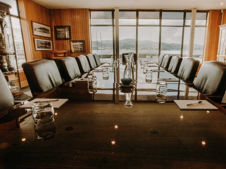Polished timber boardroom with dark leather chairs, large windows framing a harbour view