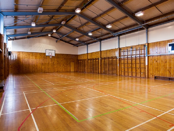Smaller indoor sports hall with timber panelled walls, court markings, and wall-mounted sports equipment