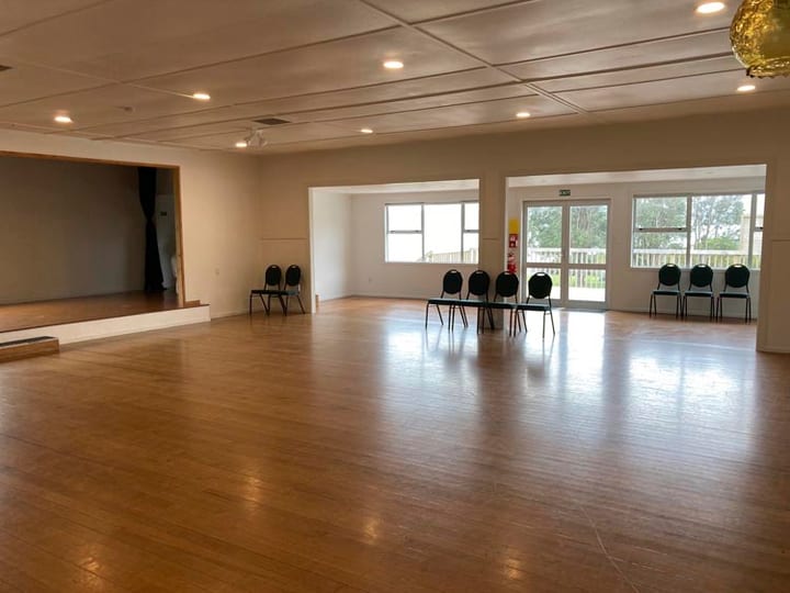 Empty community hall with timber floor, raised platform and windows