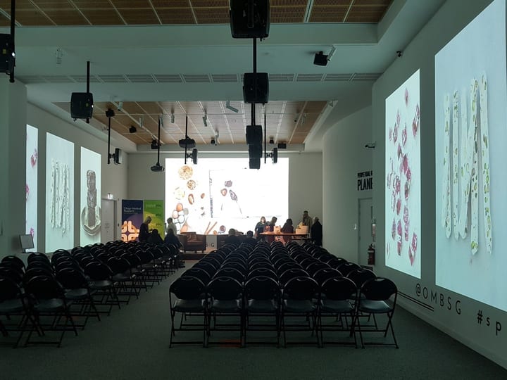 Large gallery space configured with rows of chairs facing a presentation screen