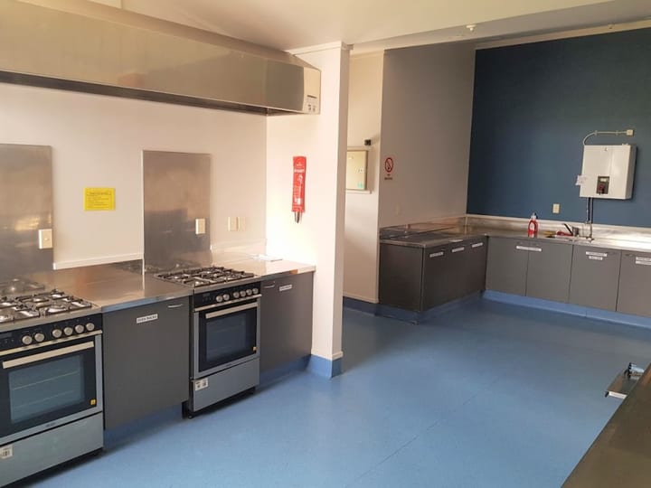 Commercial kitchen with stainless benches, two ovens, extractor hood, and blue vinyl floor