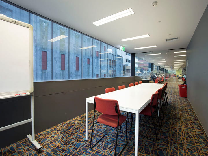Long meeting room with white table, red chairs, whiteboard and city-view windows