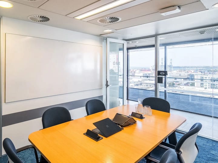 Meeting room with timber table, dark chairs, whiteboard, and full-height windows overlooking a port