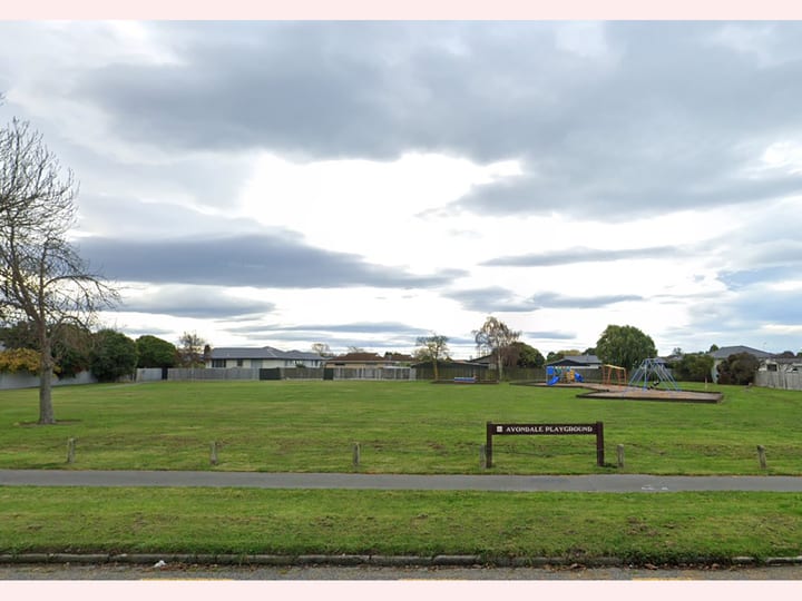 Open grass reserve with a playground area and signage near a residential street