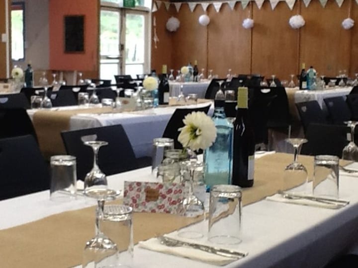 Timber hall interior set with long white-clothed tables, black chairs, and bunting near the ceiling