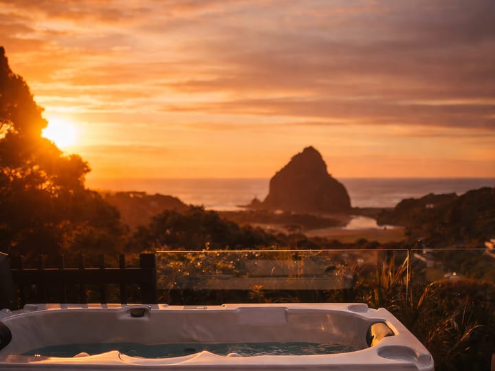 Outdoor spa pool on timber deck with rocky coastal headland view at sunset