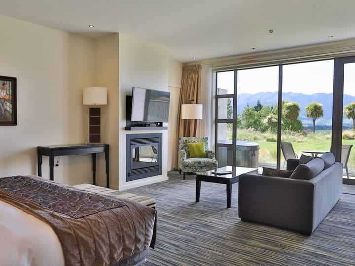 Spacious hotel suite with bed, fireplace, lounge seating and garden views through sliding doors