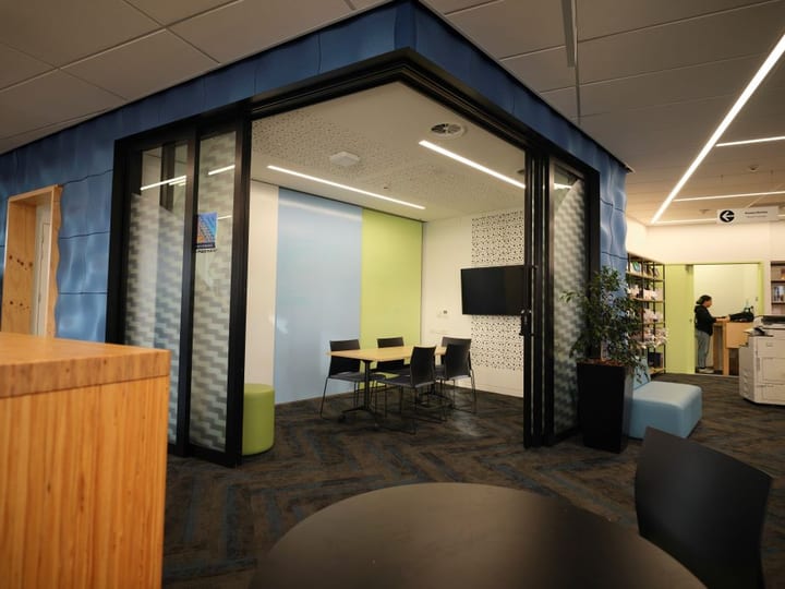 Community hub interior with glass-walled meeting room pod and open workspace beyond