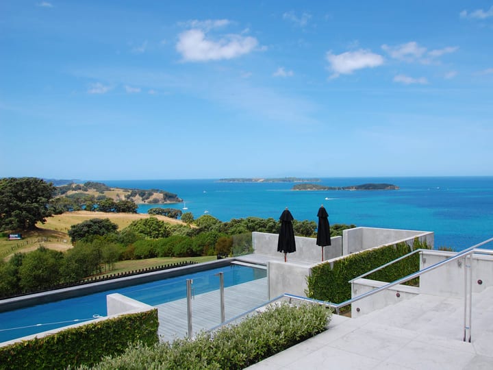 Elevated infinity pool deck with sun loungers overlooking blue bay and green hills