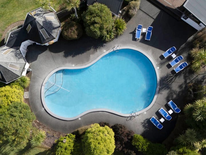 Aerial view of curved outdoor pool with sun loungers and surrounding gardens